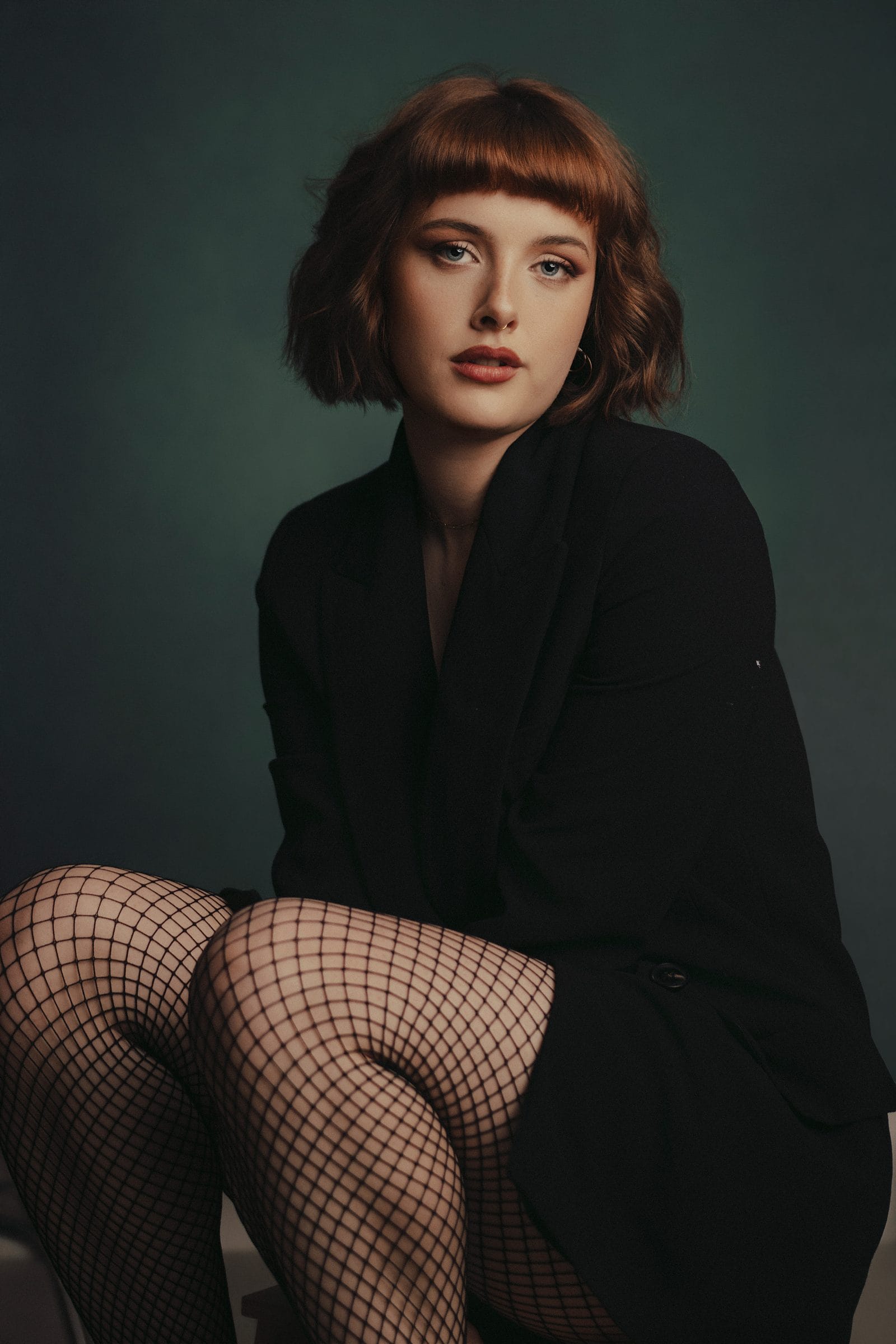Woman in a black blazer and fishnets against deep green, styling notes for what to wear to your session.