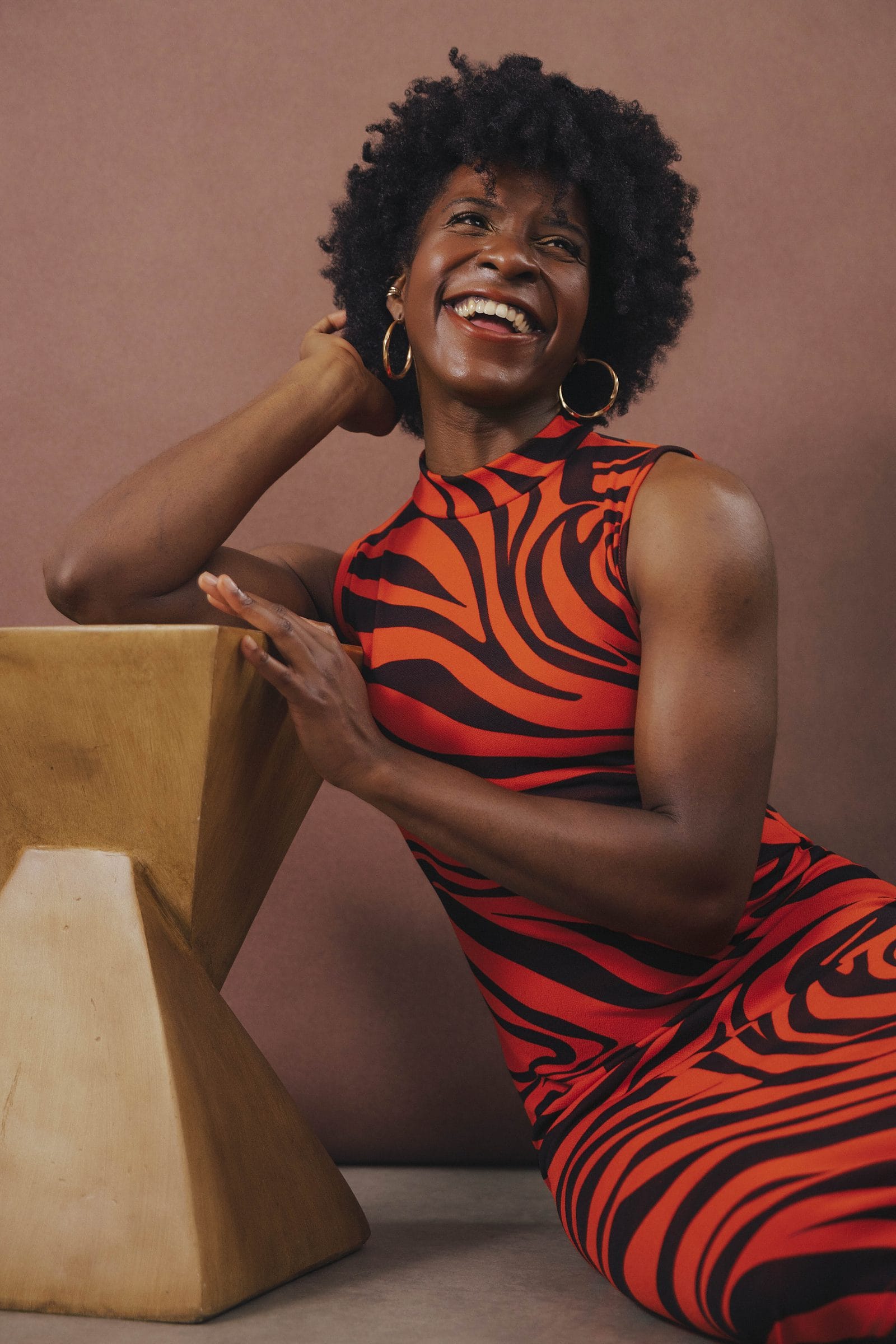 Woman in a bold red printed dress laughing freely beside a sculptural block at Body & Soul Studios, London.