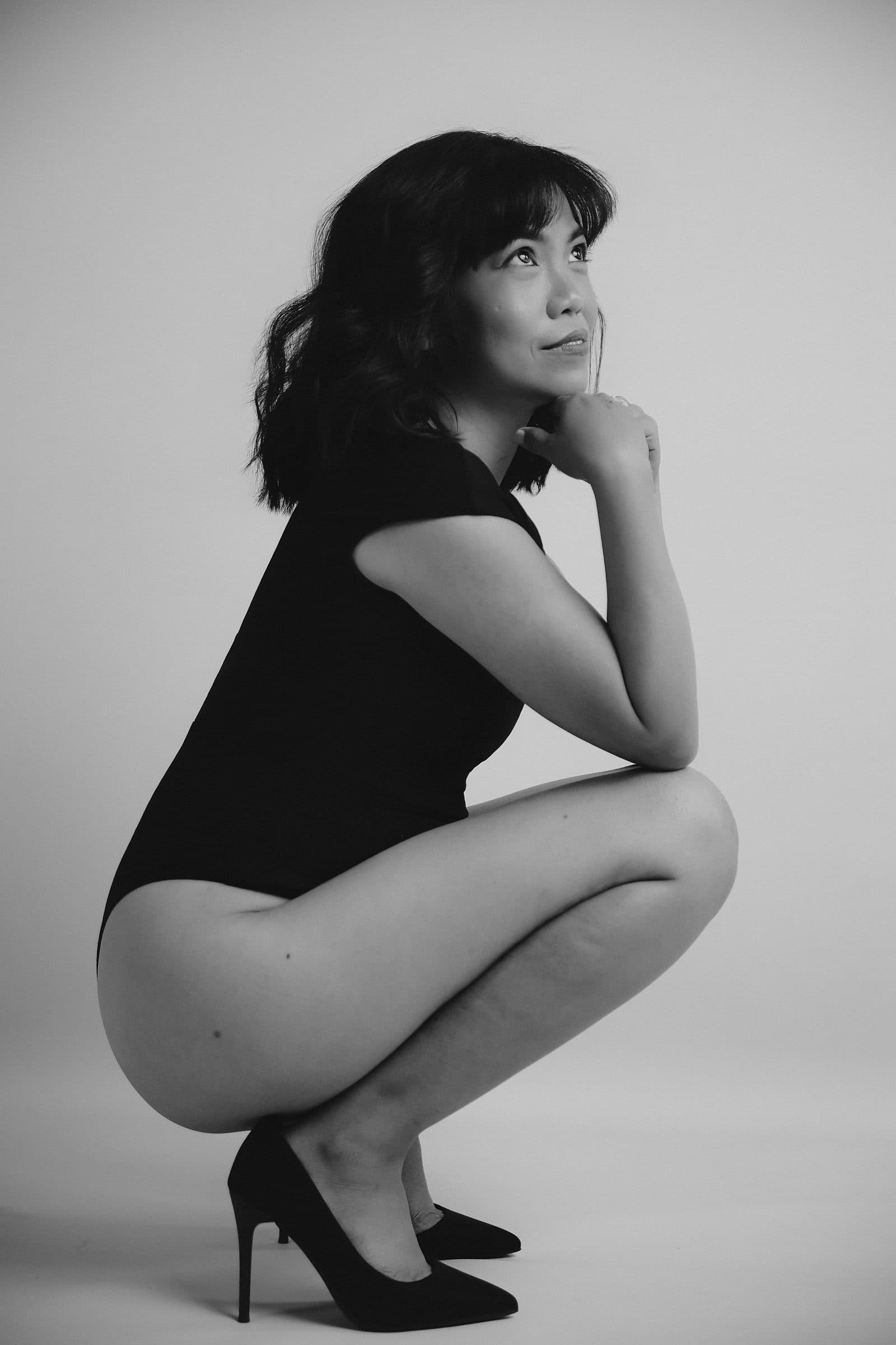 Woman crouched in a black bodysuit and heels in a striking black-and-white portrait at Body & Soul Studios, London.