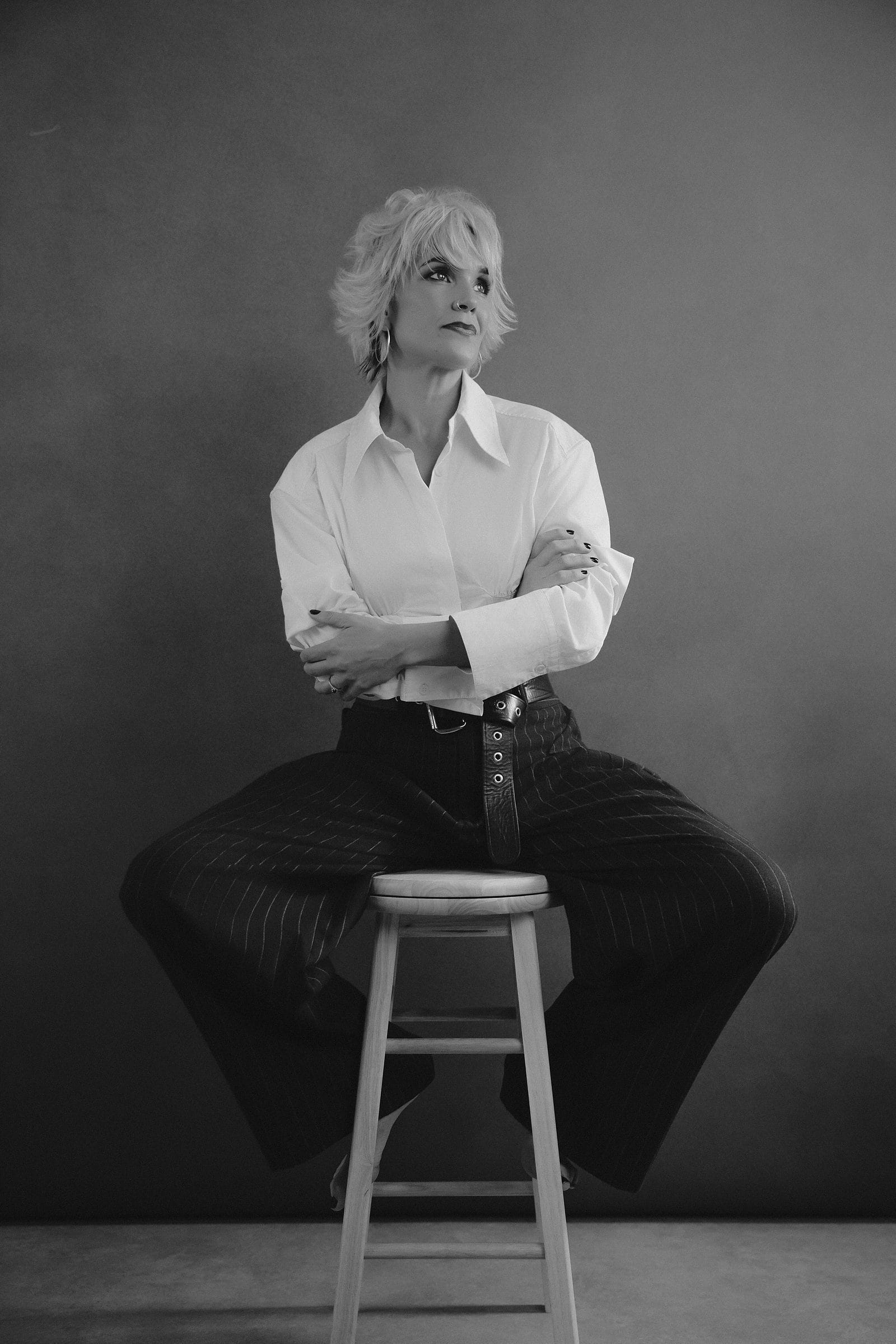 Black-and-white portrait of a woman in a crisp white shirt seated on a stool at Body & Soul Studios, London.