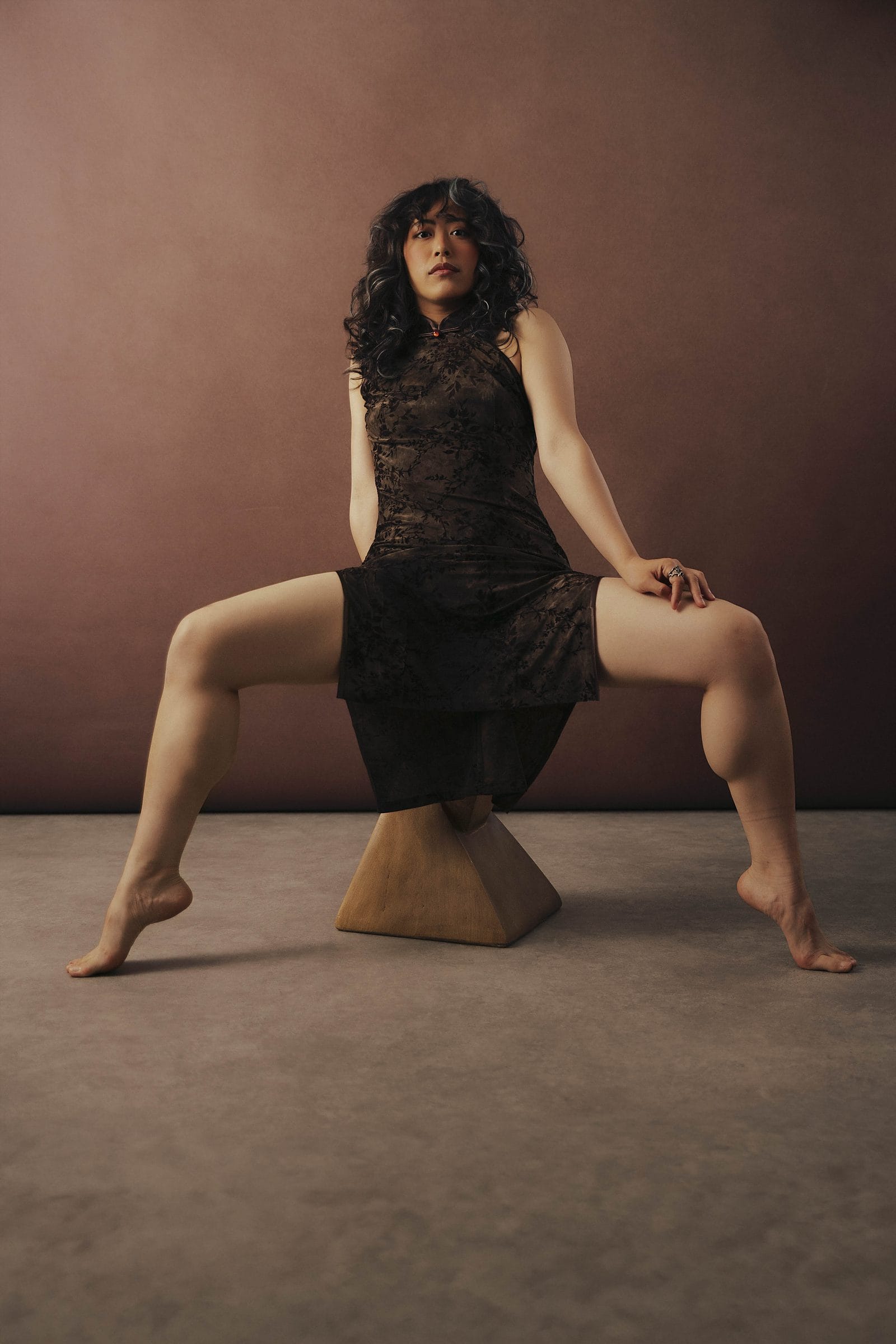 Woman in a black dress seated on a sculptural pedestal, poised and striking, at Body & Soul Studios, London.