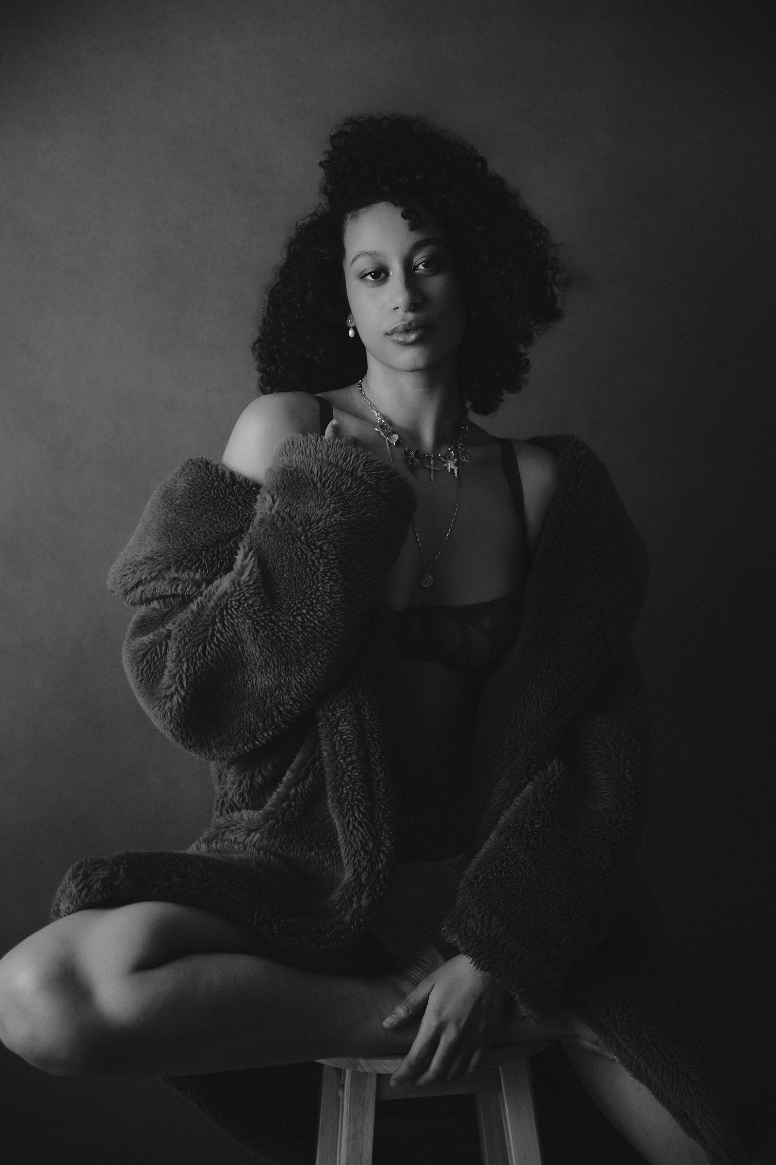 Woman seated in soft knitwear under dramatic low-key light, an intimate black-and-white portrait at Body & Soul Studios, London.