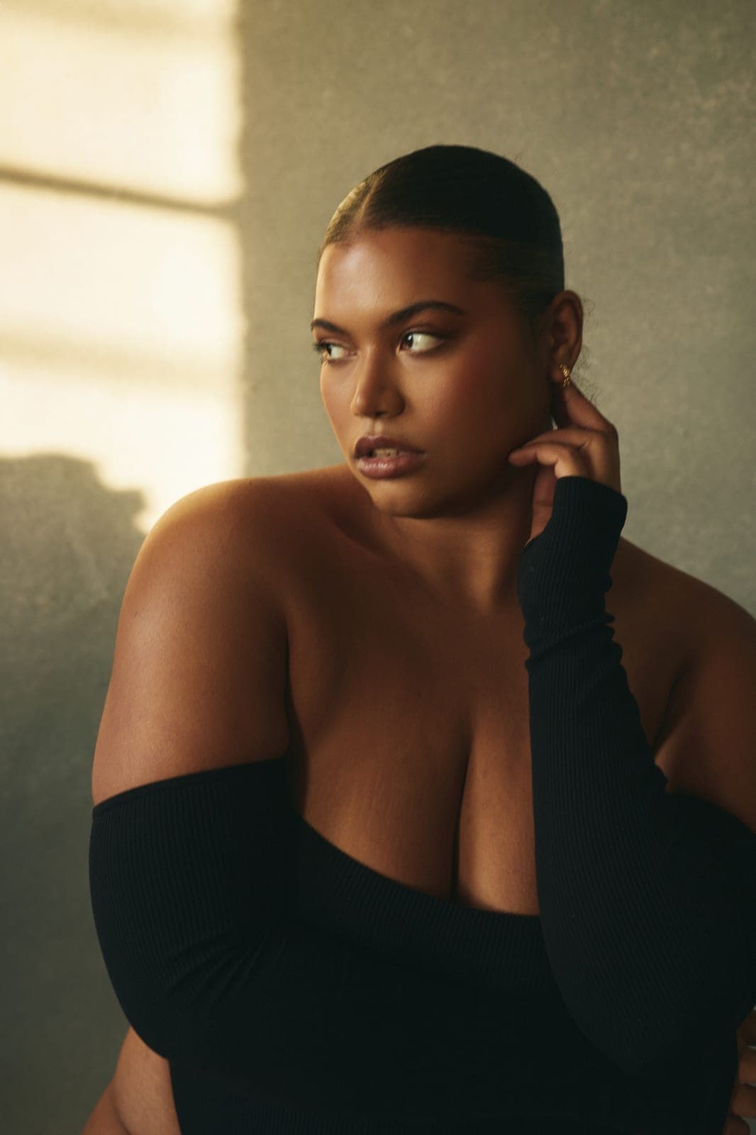 Curvy woman in an off-shoulder black top in soft window light, calm and confident, at Body & Soul Studios, London.