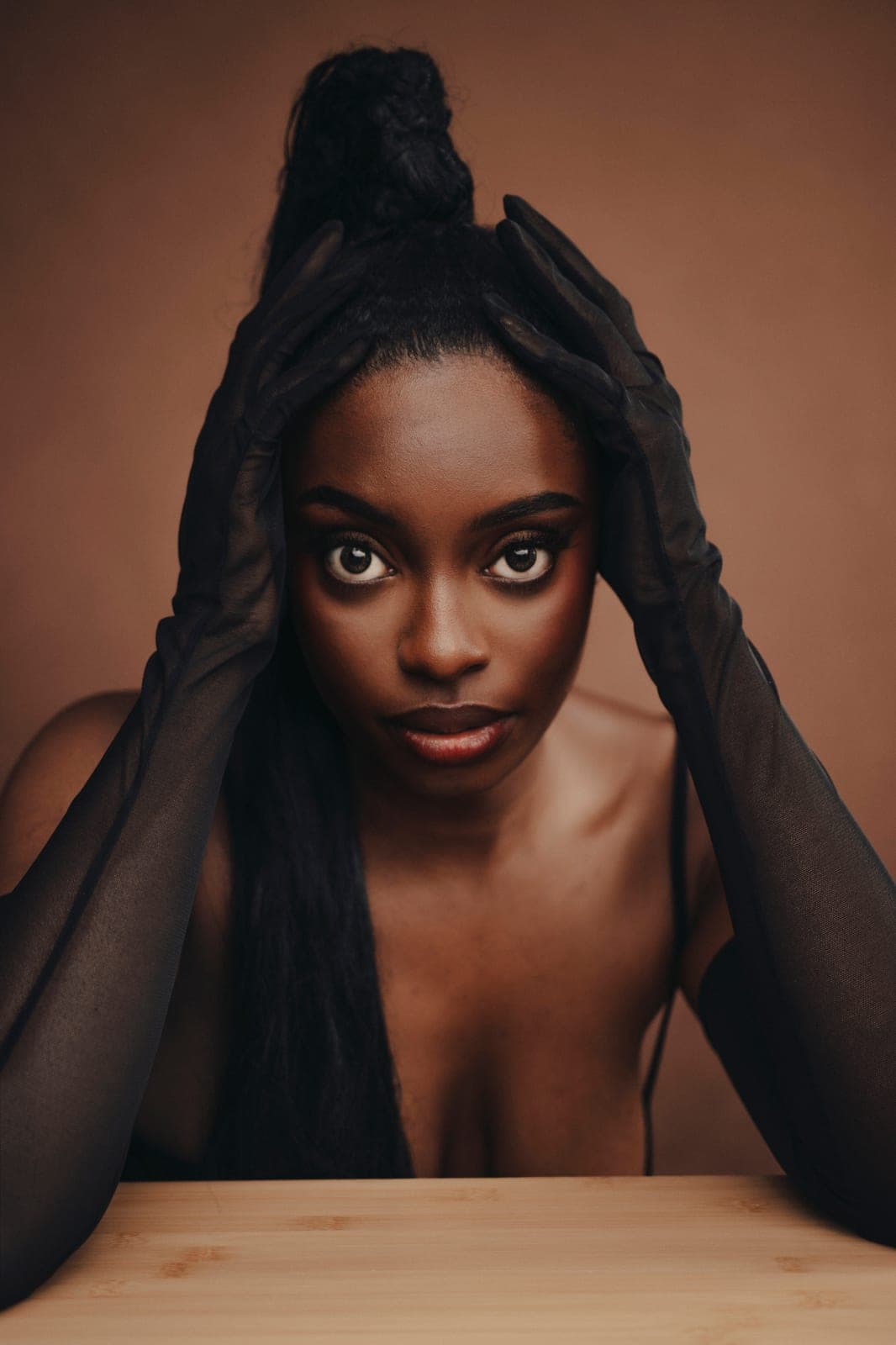 Black woman framing her face with sheer-gloved hands, a tender and direct portrait at Body & Soul Studios, London.